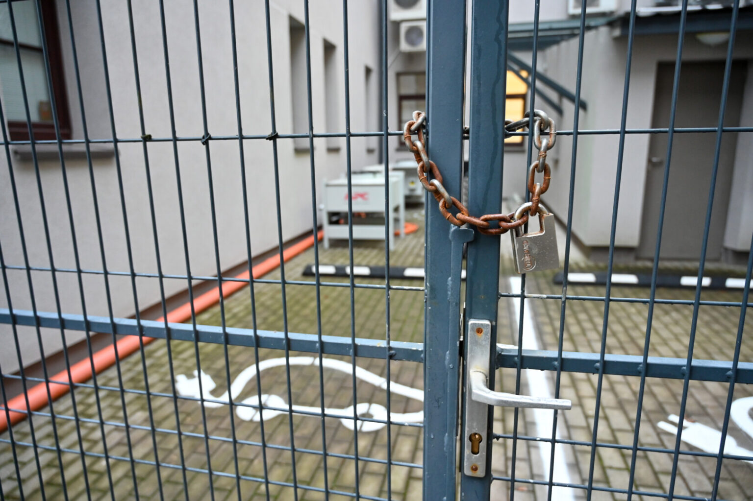 Panevėžio teritorinės ligonių kasos (TLK) kieme vasarą įrengtą elektromobilių įkrovos stotelę saugo metalinė tvora su grandine ir pakabinta spyna.