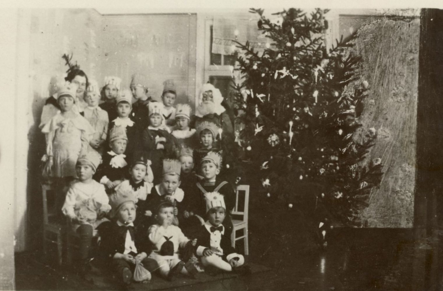 Panevėžio vaikų darželio auklėtiniai Panevėžio vaikų darželio auklėtiniai su auklėtoja T. Mažeikiene prie Kalėdų eglutės. Panevėžys. Apie 1934 metus. Panevėžio apskrities Gabrielės Petkevičaitės-Bitės viešoji biblioteka, Almonijos Marcinkevičiūtės-Bernadišienės fondas F92-90 