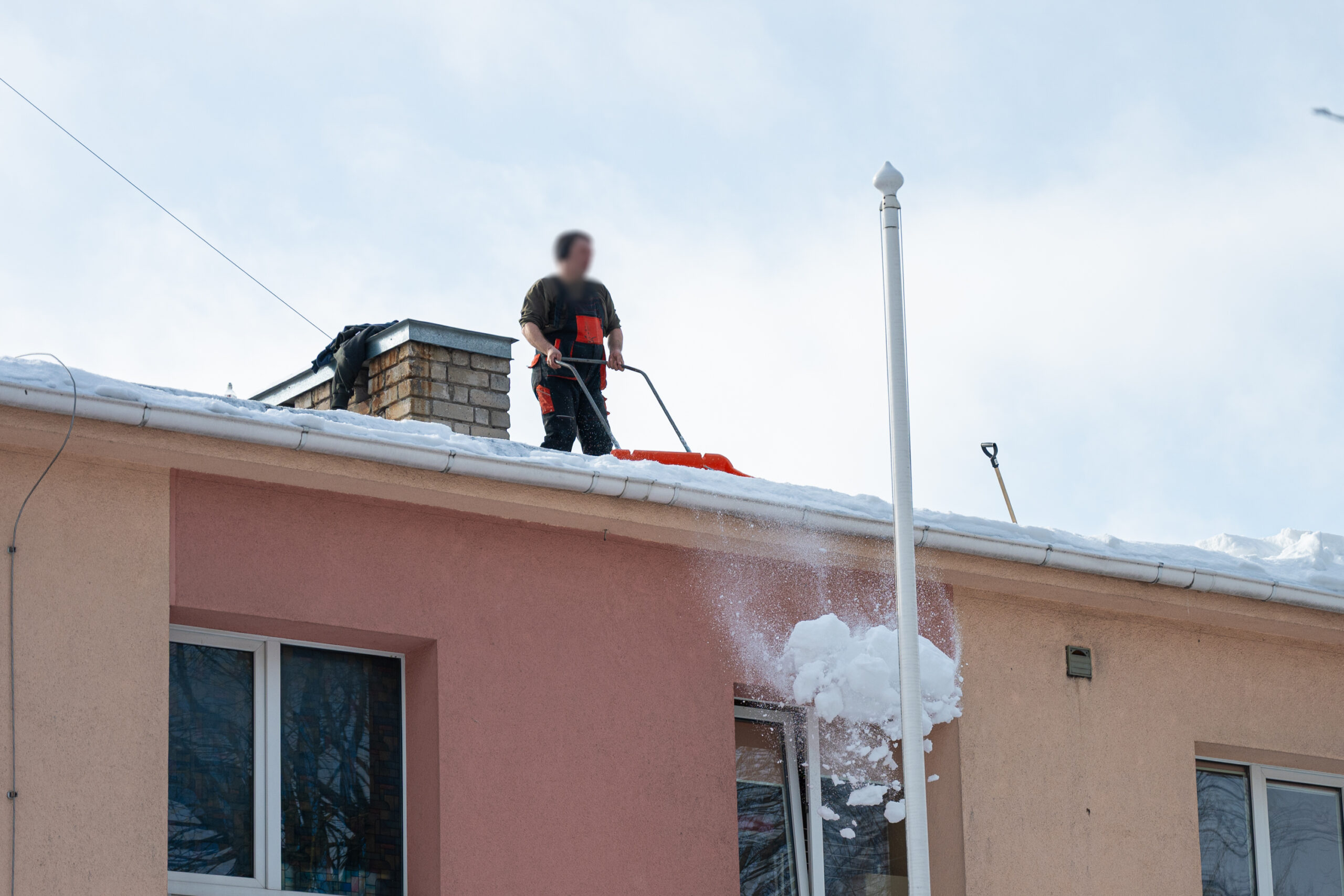 Sniegą nuo agentūros „SOS vaikai“ pastato stogo ketvirtadienį kasė už gaunamas pašalpas atidirbti atsiųstas pilietis. P. ŽIDONIO nuotr.